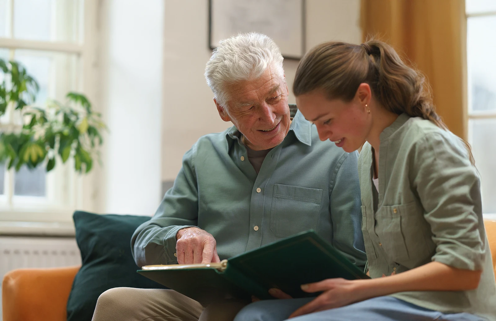 A man with white hair sits beside a young woman. They look at a book together.
