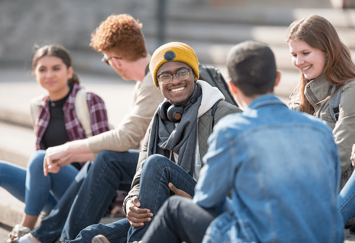 A group of students sit together on school steps, smiling and chatting with each other.