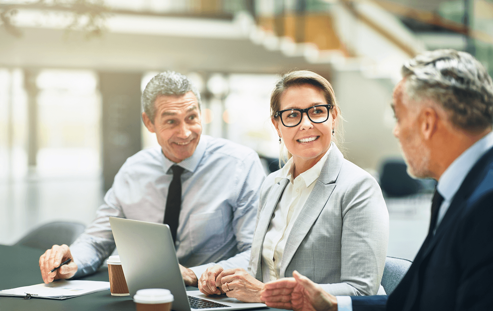 Dans une atmosphère décontractée, trois personnes habillées en tenues d’affaires discutent dans une salle éclairée.