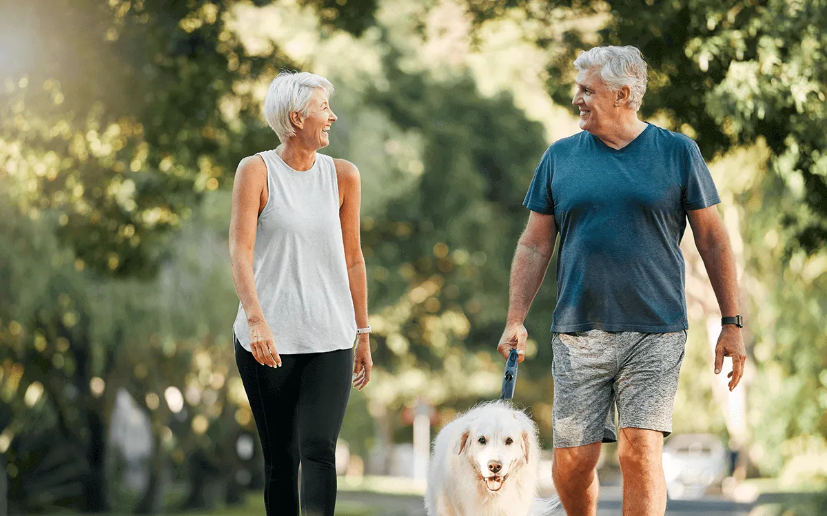 Deux aînés se sourient tout en se promenant tranquillement avec leur chien.