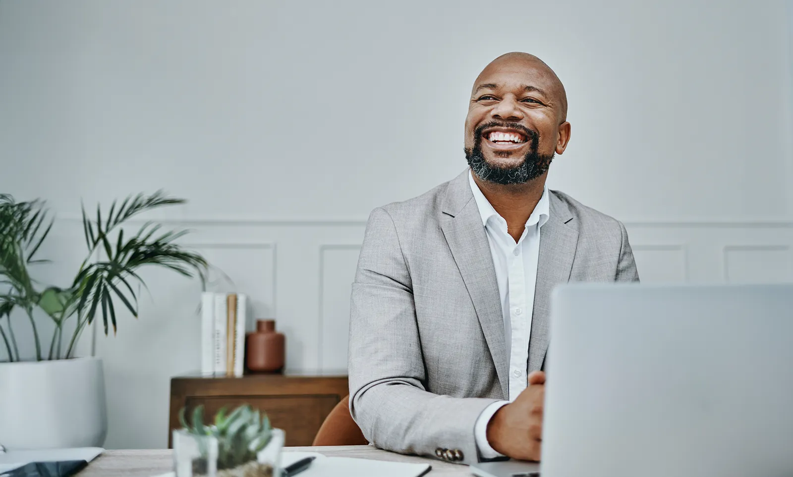 A man smiles while sitting at his desk in front of his laptop.