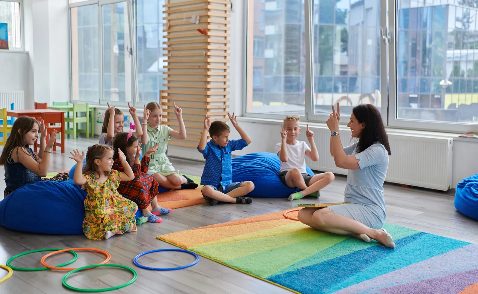 An early childhood educator plays a game with young children on the floor of a brightly lit daycare centre.