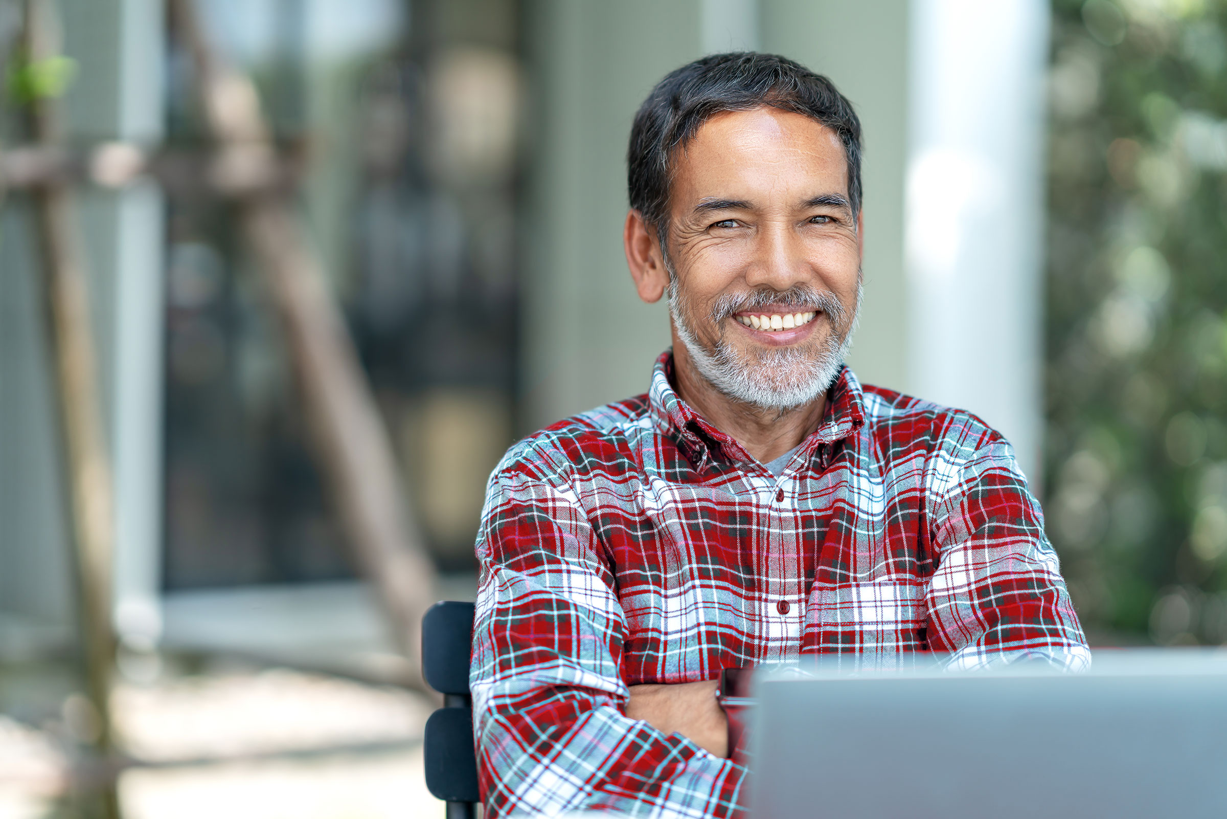A man sits outside with a laptop computer in front of him. He smiles with his arms crossed.